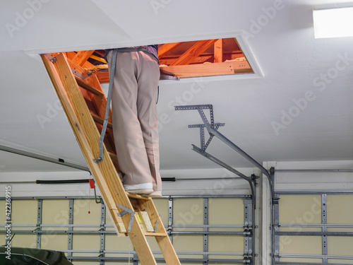 Man inspecting garage attic. Male homeowner climbing wooden pull down attic ladder stairs.