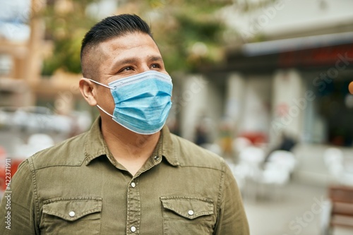 Young latin man wearing medical mask standing at the city.
