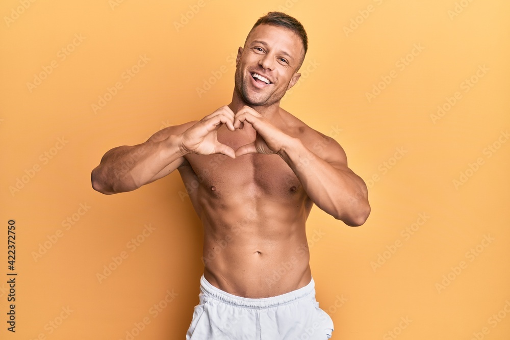 Handsome muscle man standing shirtless smiling in love showing heart symbol and shape with hands. romantic concept.