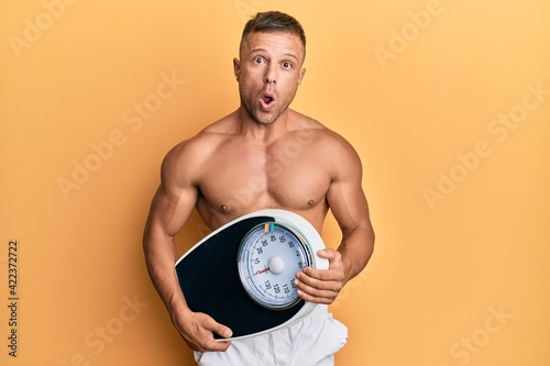 Handsome muscle man holding weight machine to balance weight loss afraid and shocked with surprise and amazed expression  fear and excited face.
