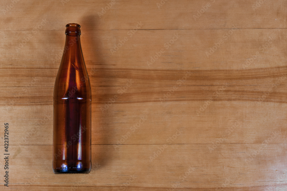 Brown glass empty beverage bottle lying vertically on wooden background - obrazy, fototapety, plakaty 