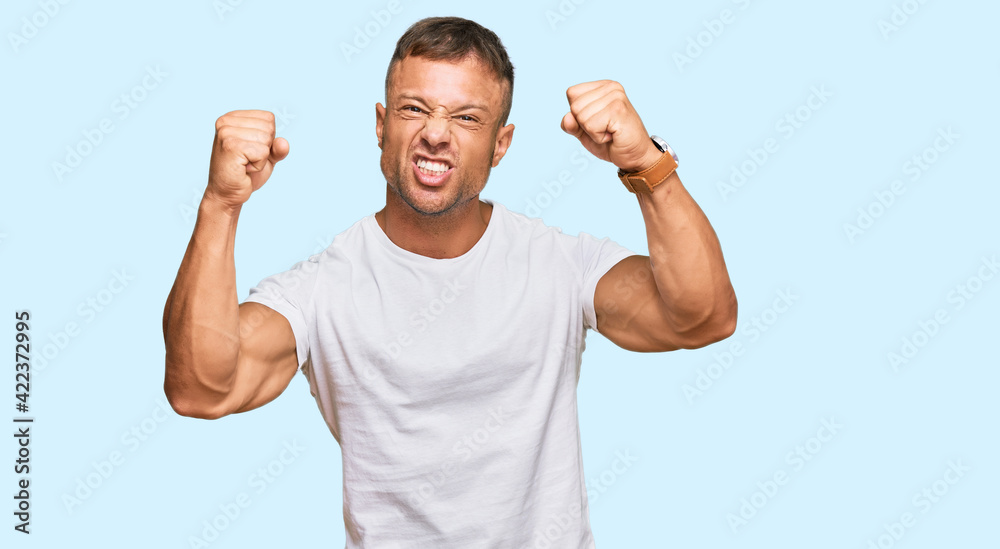 Fototapeta premium Handsome muscle man wearing casual white tshirt angry and mad raising fists frustrated and furious while shouting with anger. rage and aggressive concept.