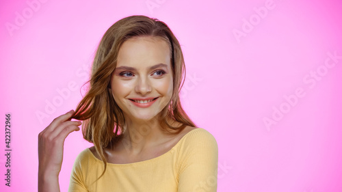 smiling young woman adjusting hair on pink