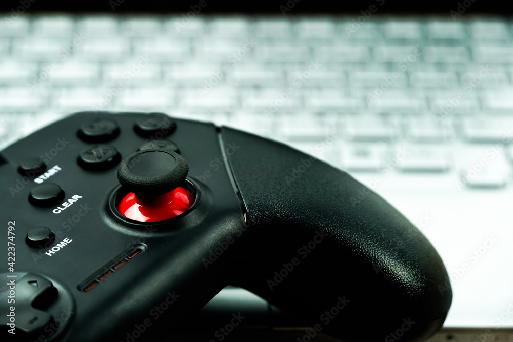 Black gamepad is lying on a laptop keyboard.The joystick for video games lies next to an open laptop. Professional gaming concept. Close-up. Black gamepad is lying on a laptop keyboard.The joystick for video games lies next to an open laptop. Professional gaming concept. Close-up.