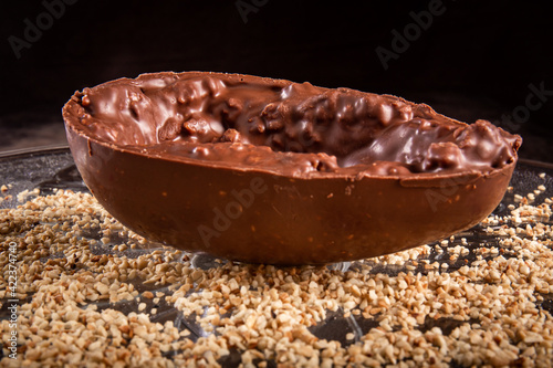 Stuffed chocolate easter egg with peanut and caramel on a wooden table with lots of peanuts around. photo