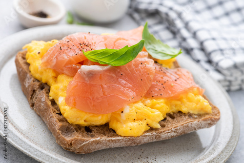 Foto Rye bread toast with scrambled eggs and smoked salmon garnished with black pepper and basil leaf