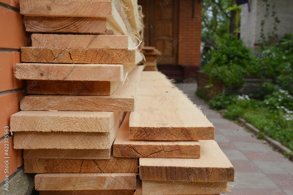 Wooden building materials: A stack of wood boards, planks and sawn timber stored near the house during house renovation. Timber stack.