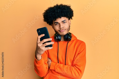 Fotografie, Obraz Young african american man with afro hair using smartphone skeptic and nervous, frowning upset because of problem