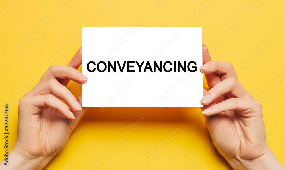 Female hands hold card paper with text Conveyancing on a yellow background. Business and finance concept Female hands hold card paper with text Conveyancing on a yellow background. Business and finance concept
