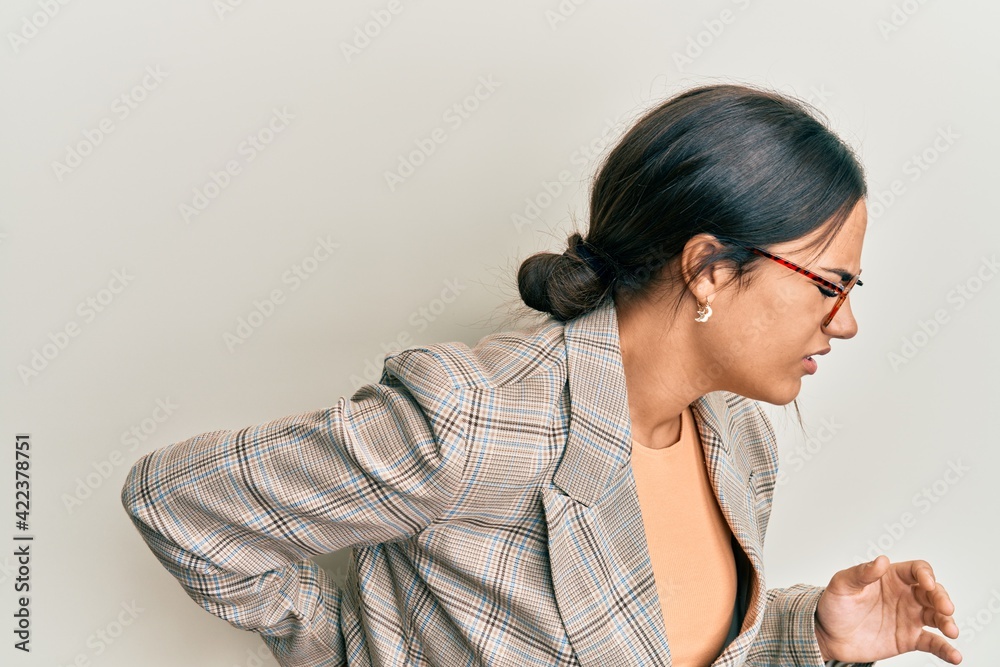 Young brunette woman wearing business jacket and glasses suffering of backache, touching back with hand, muscular pain Young brunette woman wearing business jacket and glasses suffering of backache, touching back with hand, muscular pain
