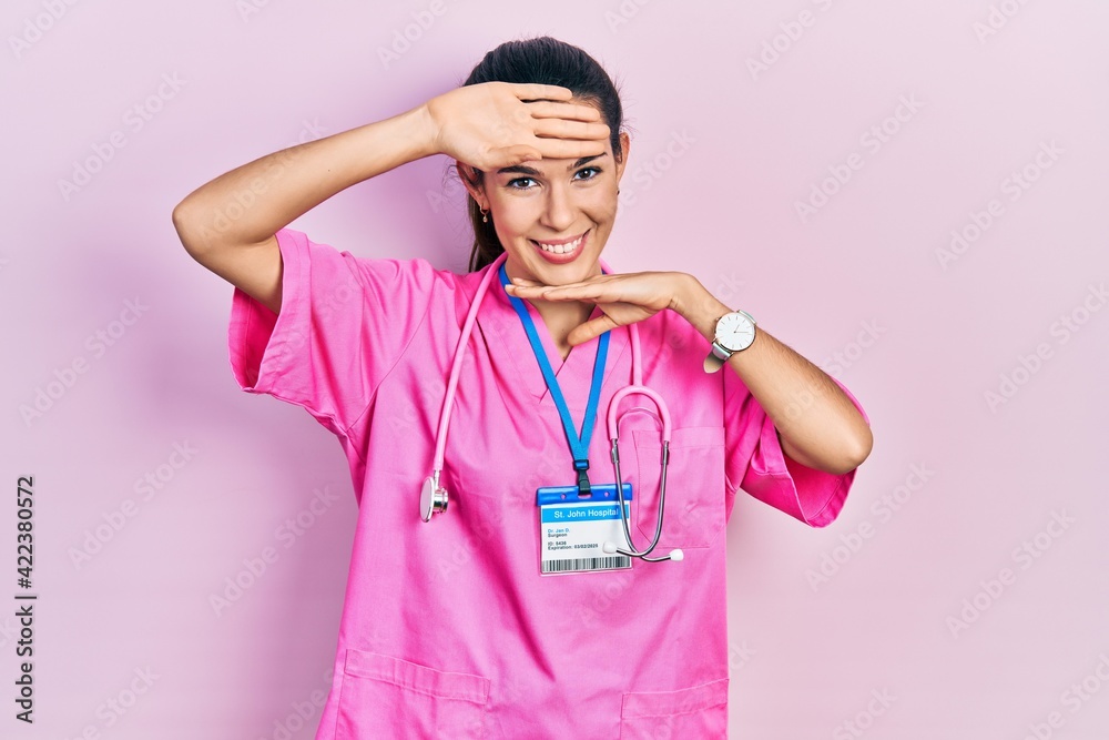 Young brunette woman wearing doctor uniform and stethoscope smiling cheerful playing peek a boo with hands showing face. surprised and exited Young brunette woman wearing doctor uniform and stethoscope smiling cheerful playing peek a boo with hands showing face. surprised and exited