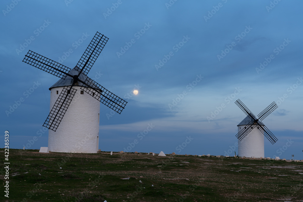 the whitewashed windmills of La Mancha in Spain under an evening sky with a full moon on the rise