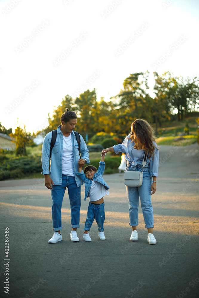 happy young family with a child walking in the park at sunset. Family in denim clothes and white shoes. The concept of a happy family. Parents hold the boys hands happy young family with a child walking in the park at sunset. Family in denim clothes and white shoes. The concept of a happy family. Parents hold the boys hands