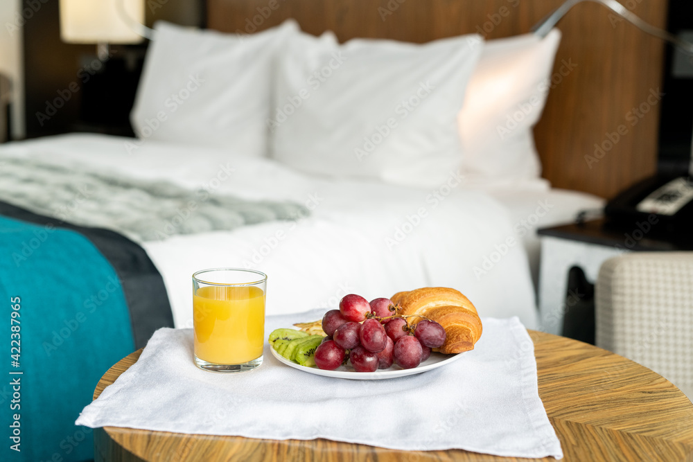 Tray with breakfast standing on small wooden table in front of camera against bed inside one of rooms of contemporary luxurious hotel Tray with breakfast standing on small wooden table in front of camera against bed inside one of rooms of contemporary luxurious hotel