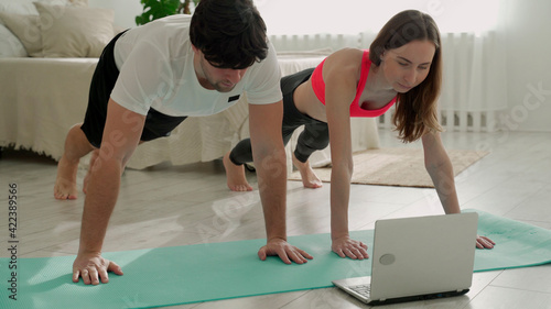 Sporty couple in sportswear doing exercise having online workout together at home