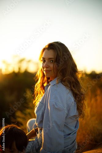 happy girl smiling at the top of the hill at sunset. the face of a woman with wavy hair is bathed in sunlight. happy young girl outside 