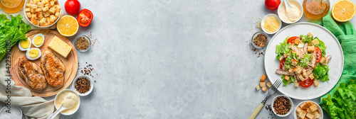 A culinary banner with a ready-made Caesar salad and ingredients for its preparation on a gray background.