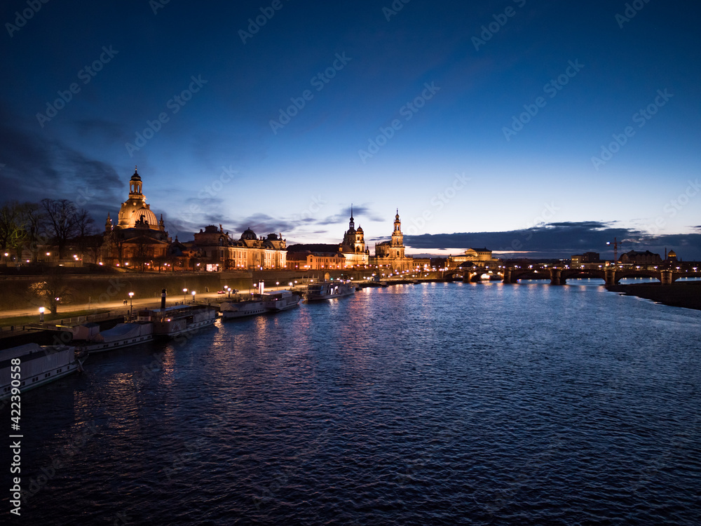 Dresden city elbe river after sunset in the blue hour. Illuminated skyline when the sun is going down in the evening. Beautiful old buildings and steamboats in the cityscape.