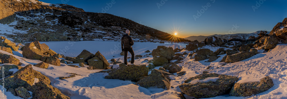 panoramic view of the sunrise or sunset of the sun over the mountains with a snow lake with a unrecognized person