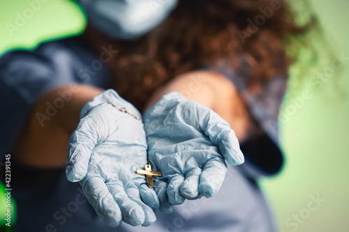 young female nurse wearing a surgical mask and surgical gloves is holding a crucifix in her hand