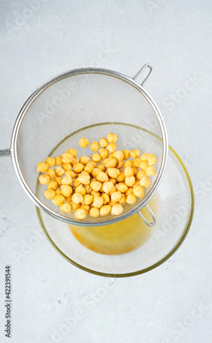 Chickpea water aquafaba. Egg replacement. Vegan concept. Metal sieve draining aquafaba chickpea water into glass bowl. on a gray background. sustainable lifestyle and natural eco-friendly products.