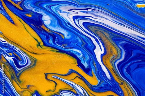 Fluid art texture. Backdrop with abstract swirling paint effect. Liquid acrylic artwork with flows and splashes. Mixed paints for baner or wallpaper. Blue, golden and white overflowing colors.