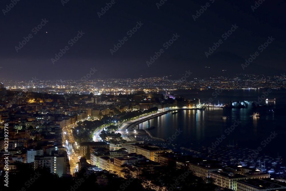 Panorama of the Gulf of Naples at night the metropolitan city with a thousand colors and reflections on the sea and in the background the stars and Vesuvius