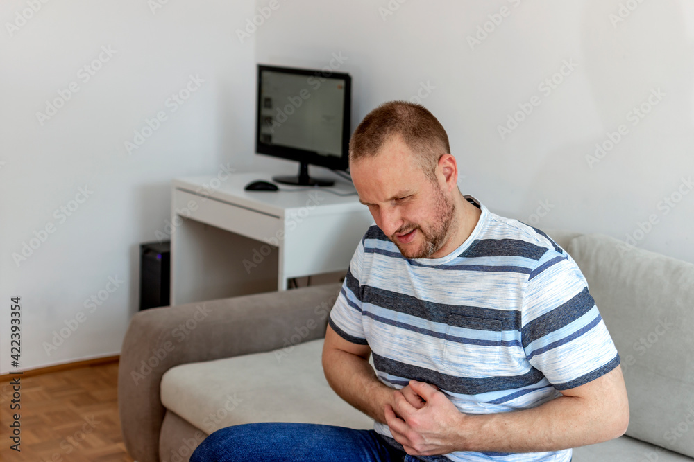 Unhappy man suffering from stomach ache at home. Shot of a young man experiencing stomach pain while sitting on the sofa at home. People, healthcare and problems concept.