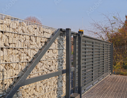 Gabion. Automatic entrance gate used in combination with a wall made of gabion.