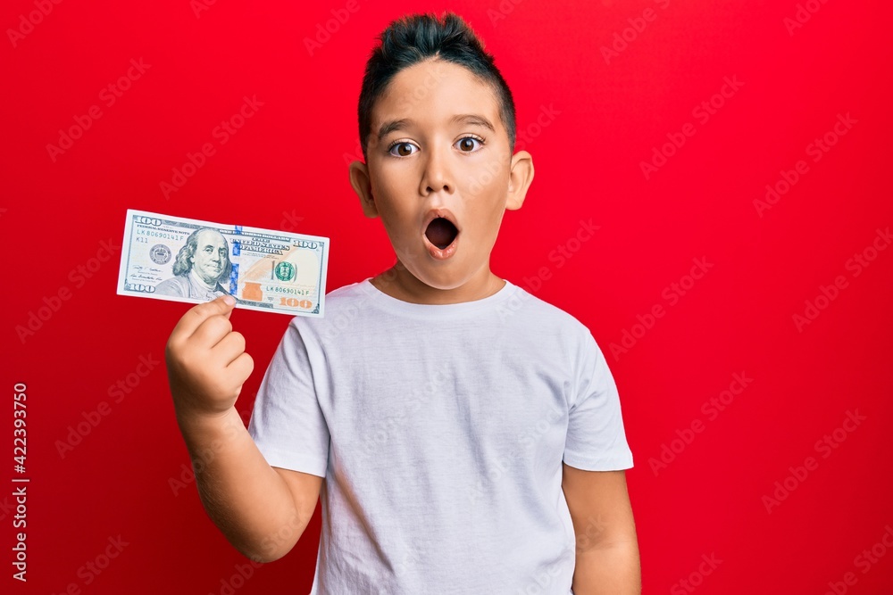 Little boy hispanic kid holding 100 dollars banknote scared and amazed with open mouth for surprise, disbelief face Little boy hispanic kid holding 100 dollars banknote scared and amazed with open mouth for surprise, disbelief face