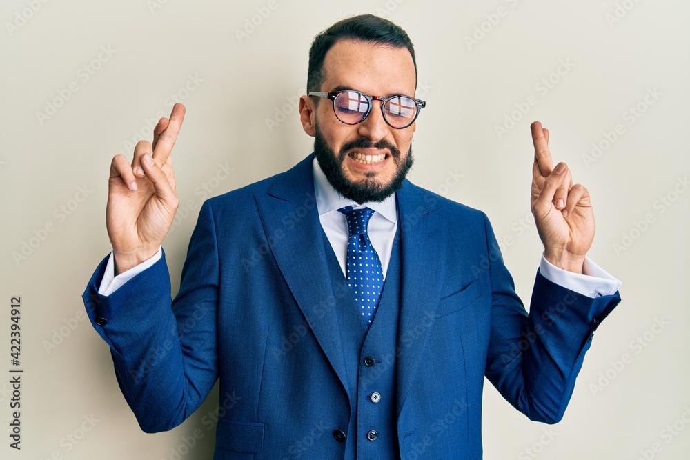 Young man with beard wearing business suit and tie gesturing finger crossed smiling with hope and eyes closed. luck and superstitious concept. Young man with beard wearing business suit and tie gesturing finger crossed smiling with hope and eyes closed. luck and superstitious concept.