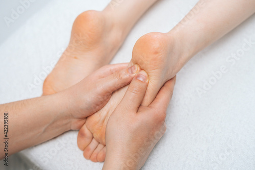 Male masseur massaging feet to young relaxing woman lying on massage table, close-up. Professional physiotherapist with strong hands performing foot massage. Concept of massage spa treatments