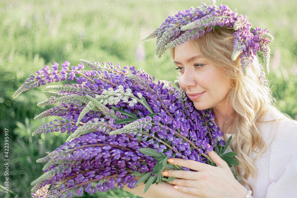 A hippy girl holding bouquet of wildflowers in her hands. Girl hid her face behind bouquet of lupins. Girl holds large bouquet of purple lupins in a flowering field. Nature concept. Present A hippy girl holding bouquet of wildflowers in her hands. Girl hid her face behind bouquet of lupins. Girl holds large bouquet of purple lupins in a flowering field. Nature concept. Present