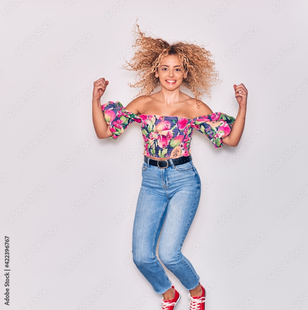 Young beautiful curly girl wearing casual clothes smiling happy. Jumping with smile on face celebrating with fists up over isolated white background. Young beautiful curly girl wearing casual clothes smiling happy. Jumping with smile on face celebrating with fists up over isolated white background.