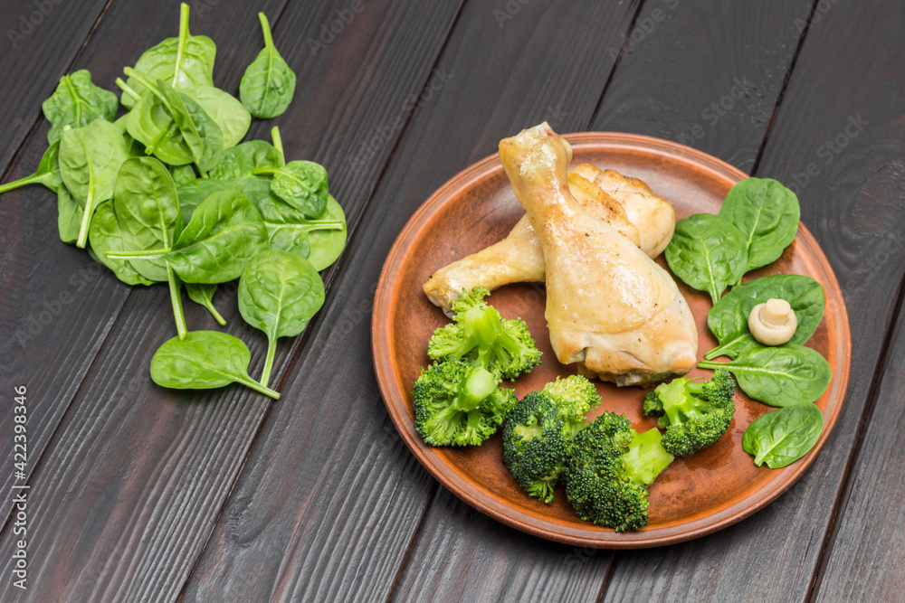 Chicken meat with broccoli and spinach on ceramic plate. Spinach leaves on table. Top view. Chicken meat with broccoli and spinach on ceramic plate. Spinach leaves on table. Top view.