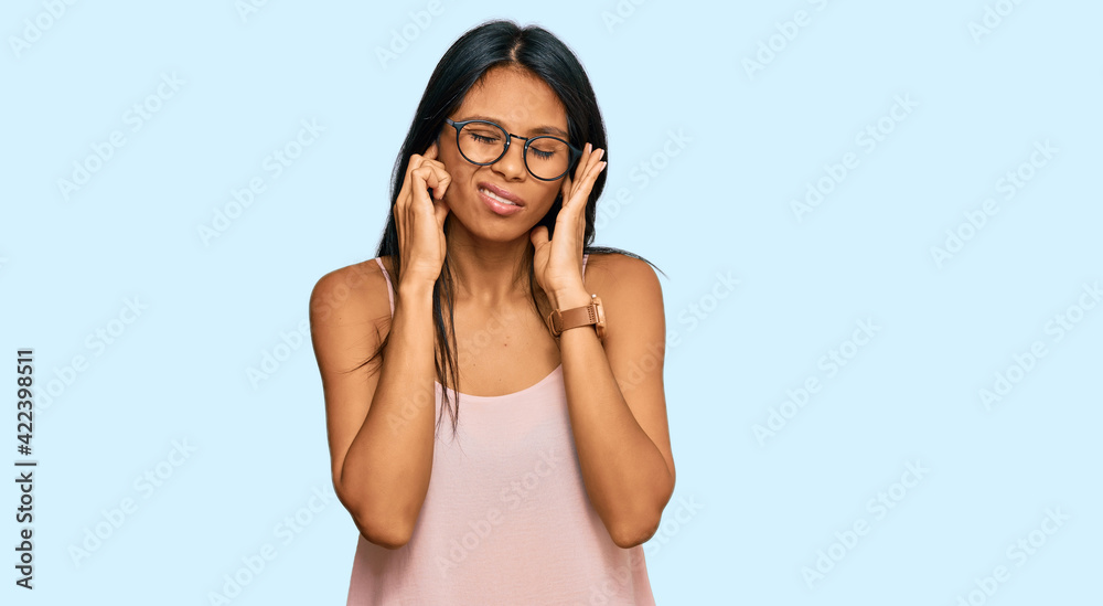 Young african american woman wearing casual clothes and glasses covering ears with fingers with annoyed expression for the noise of loud music. deaf concept. Young african american woman wearing casual clothes and glasses covering ears with fingers with annoyed expression for the noise of loud music. deaf concept.