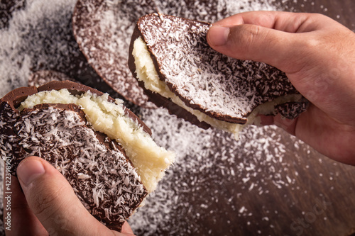 Hands take a cracked chocolate easter egg with coconut filling and grated coconut on the top on a wooden table.