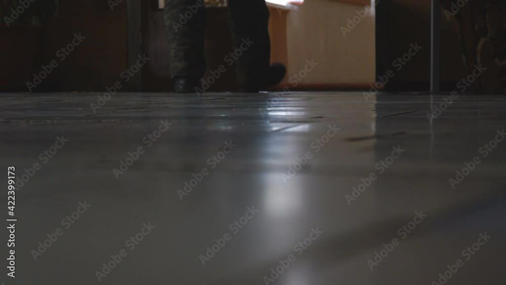 The feet of a man in sneakers walking down a corridor in a dark room. Low angle view. Low key The feet of a man in sneakers walking down a corridor in a dark room. Low angle view. Low key