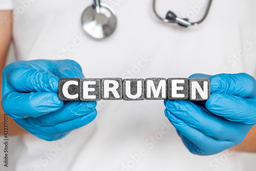 cerumen - word from stone blocks with letters holding by a doctor's hands in medical protective gloves. technical term for earwax.