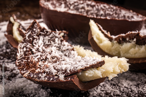 Canvas Print Close up of a cracked chocolate easter egg with coconut filling and grated coconut on the top on a wooden table