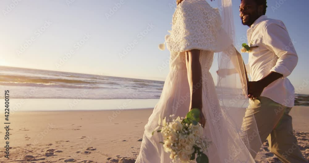 African american couple in love getting married, holding hands on the beach at sunset