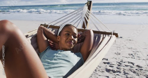African american woman smiling and lying in hammock on the beach