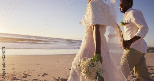 African american couple in love getting married, holding hands on the beach at sunset