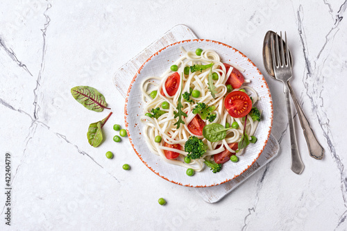 A dish of Asian cuisine. Udon noodles with cherry tomatoes, broccoli and green pea