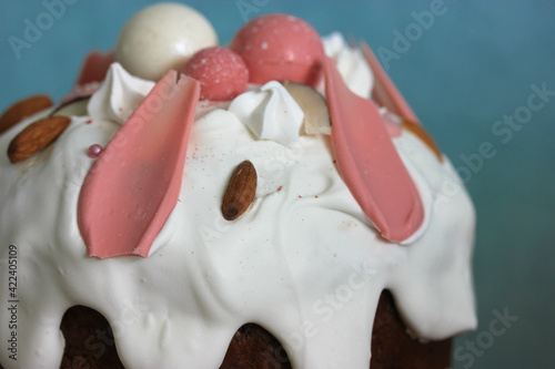 Easter cake decorated with white icing, meringue, pink decorative chocolate balls, nuts. Homemade Easter bread top view on blue background. A recipe for a traditional Easter cake.