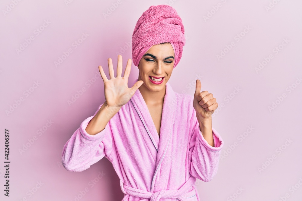 Young man wearing woman make up wearing shower towel on head and bathrobe showing and pointing up with fingers number six while smiling confident and happy. Young man wearing woman make up wearing shower towel on head and bathrobe showing and pointing up with fingers number six while smiling confident and happy.