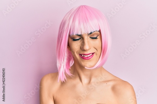 Young man wearing woman make up wearing pink wig looking confident at the camera smiling with crossed arms and hand raised on chin. thinking positive.