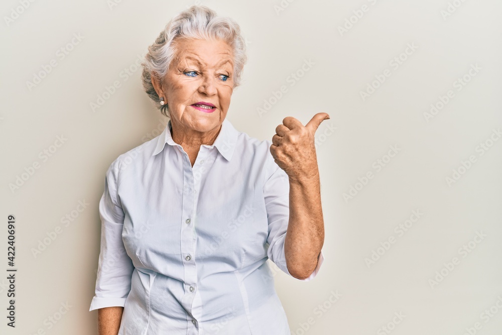 Senior grey-haired woman wearing casual clothes pointing thumb up to the side smiling happy with open mouth