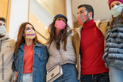 Community of young people wearing trendy face mask walking together arm on shoulders - friends together against coronavirus, unity and trust concept during covid-19 pandemic.