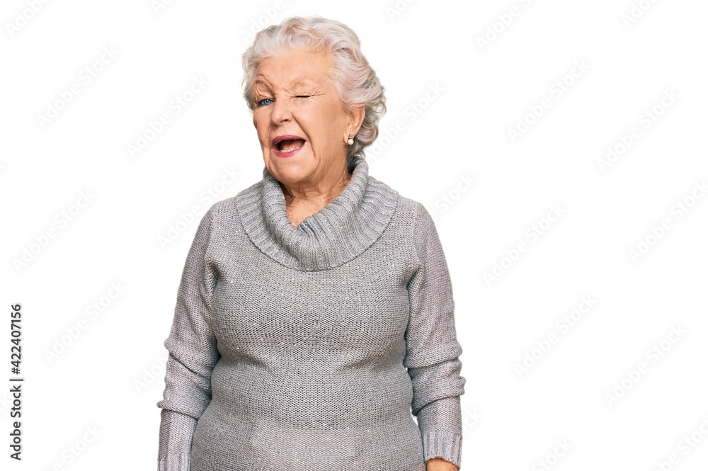 Senior grey-haired woman wearing casual winter sweater winking looking at the camera with sexy expression, cheerful and happy face. Senior grey-haired woman wearing casual winter sweater winking looking at the camera with sexy expression, cheerful and happy face.
